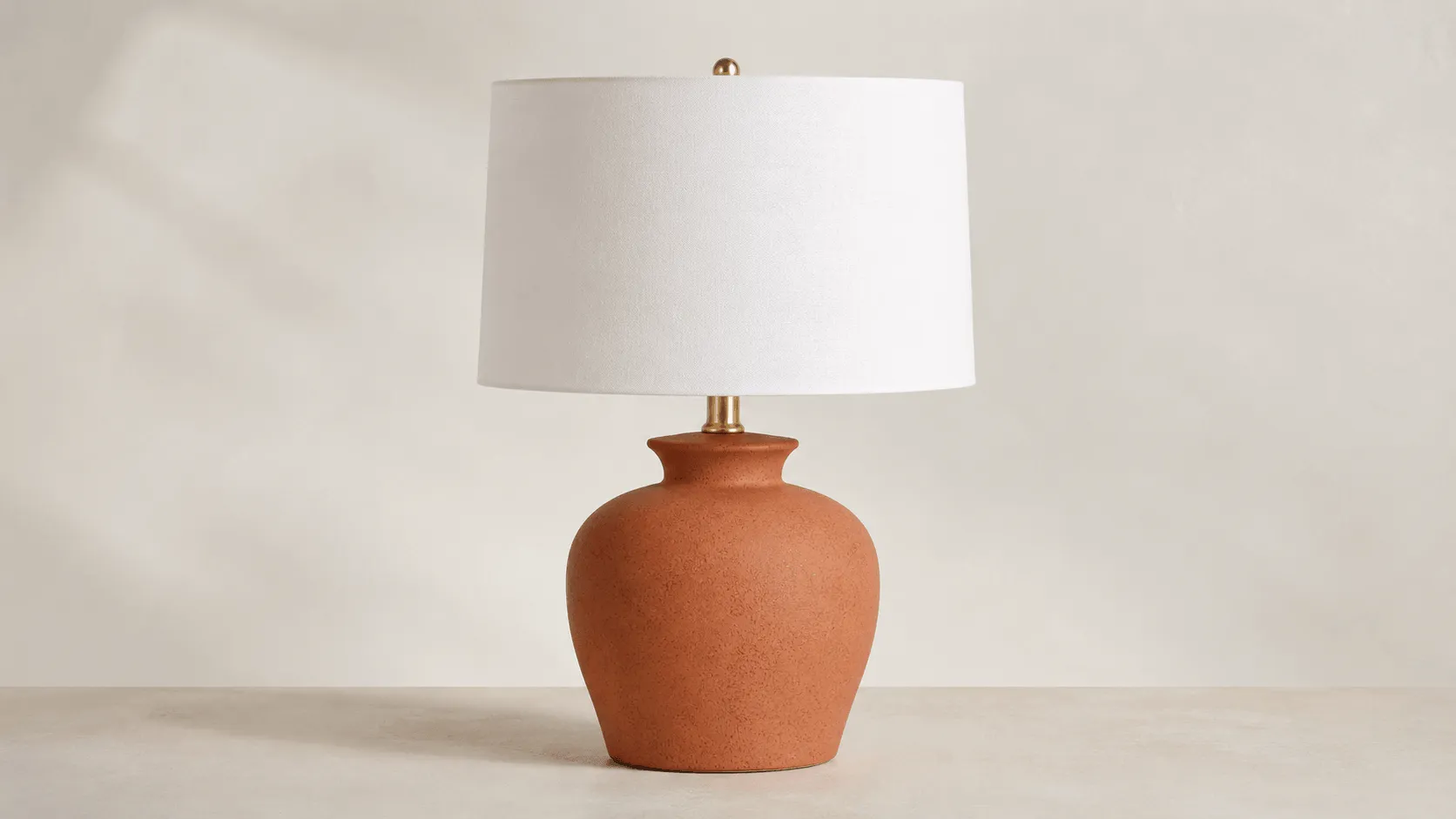 Modern ceramic decor example with a large rounded terracotta-red table lamp body and wide white shade